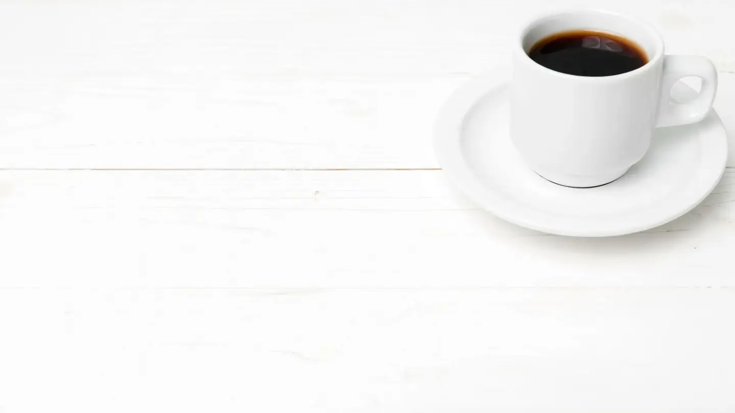 The same photo after Edit by prompt: only the cup of coffee on its saucer remains on the white wooden table