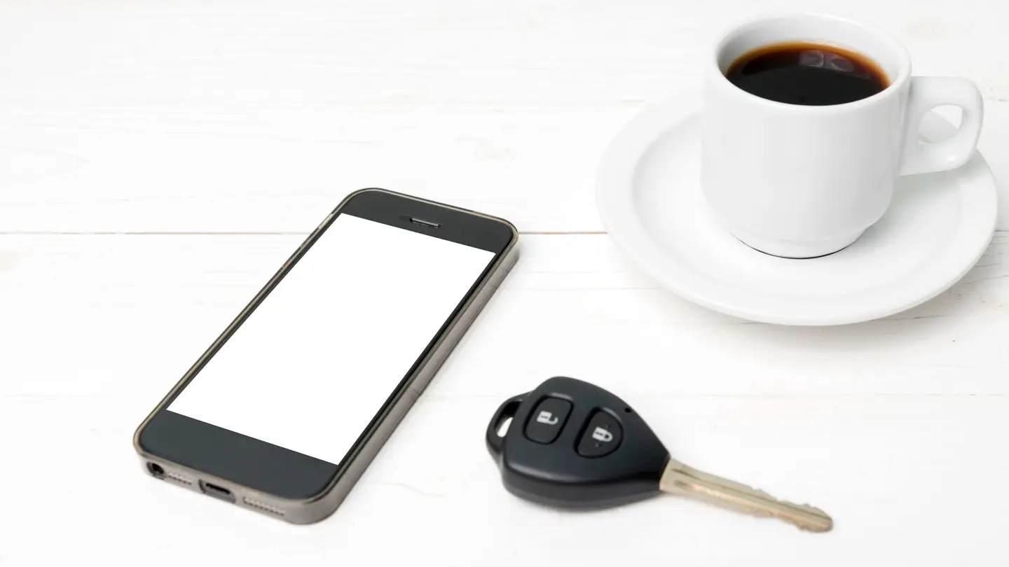 The original stock photo: a white cup of black coffee on a saucer, a smartphone and a car key on a white wooden table