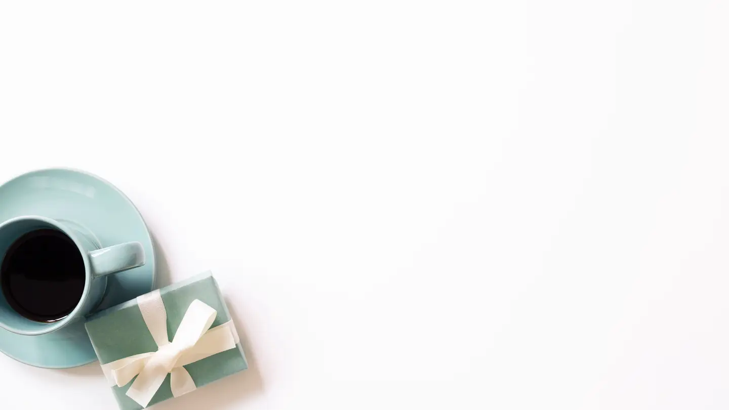 A teal coffee cup on a saucer and a small wrapped gift on a plain white background