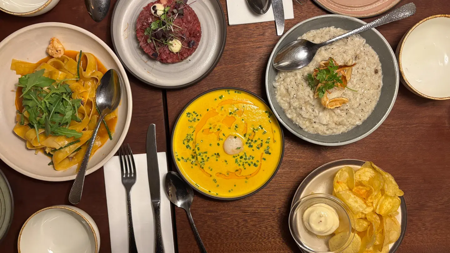 An overhead view of a restaurant table with pasta, steak tartare, pumpkin soup, risotto and potato chips